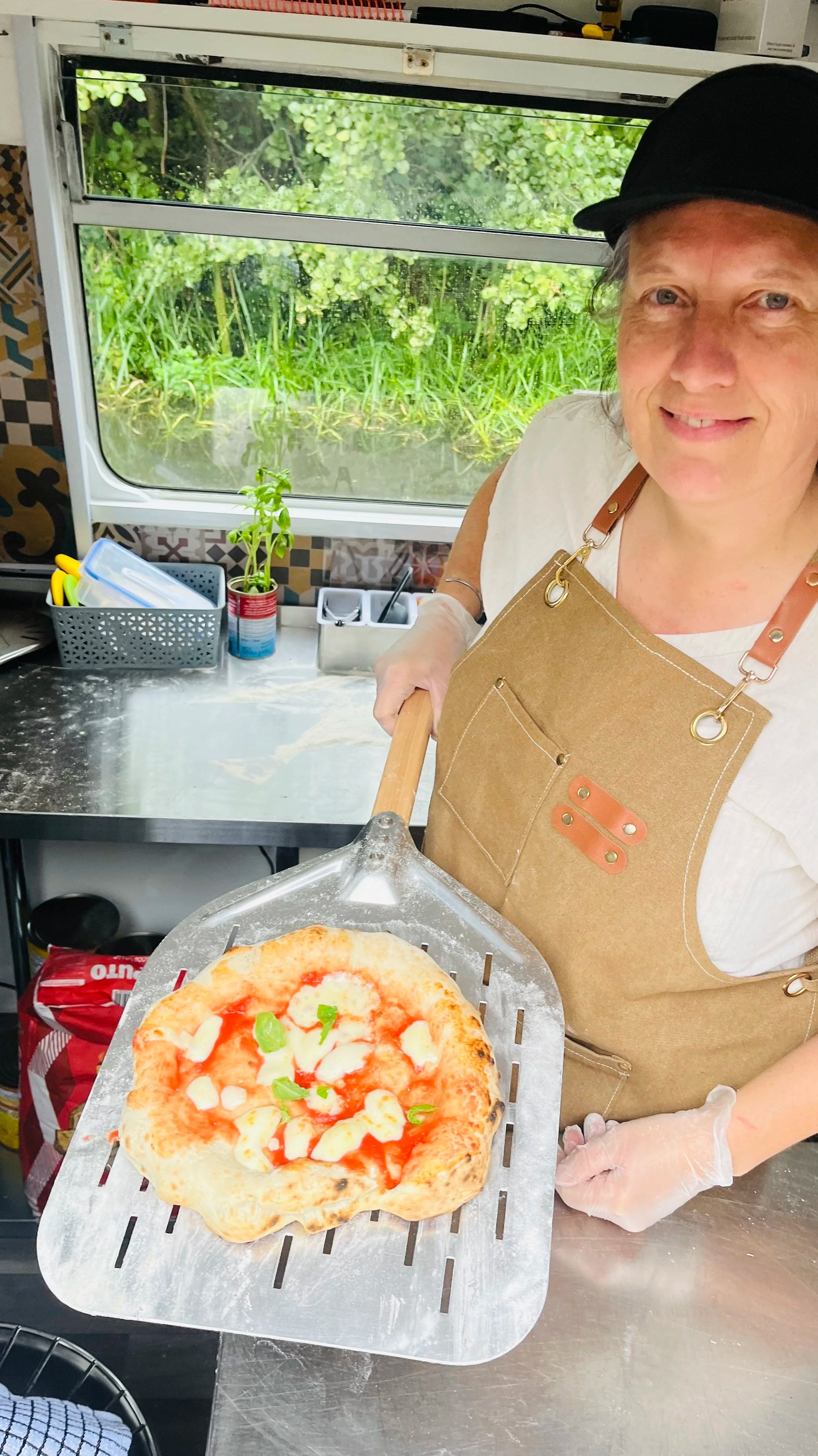 Person holding a pizza on a metal spatula in a kitchen setting